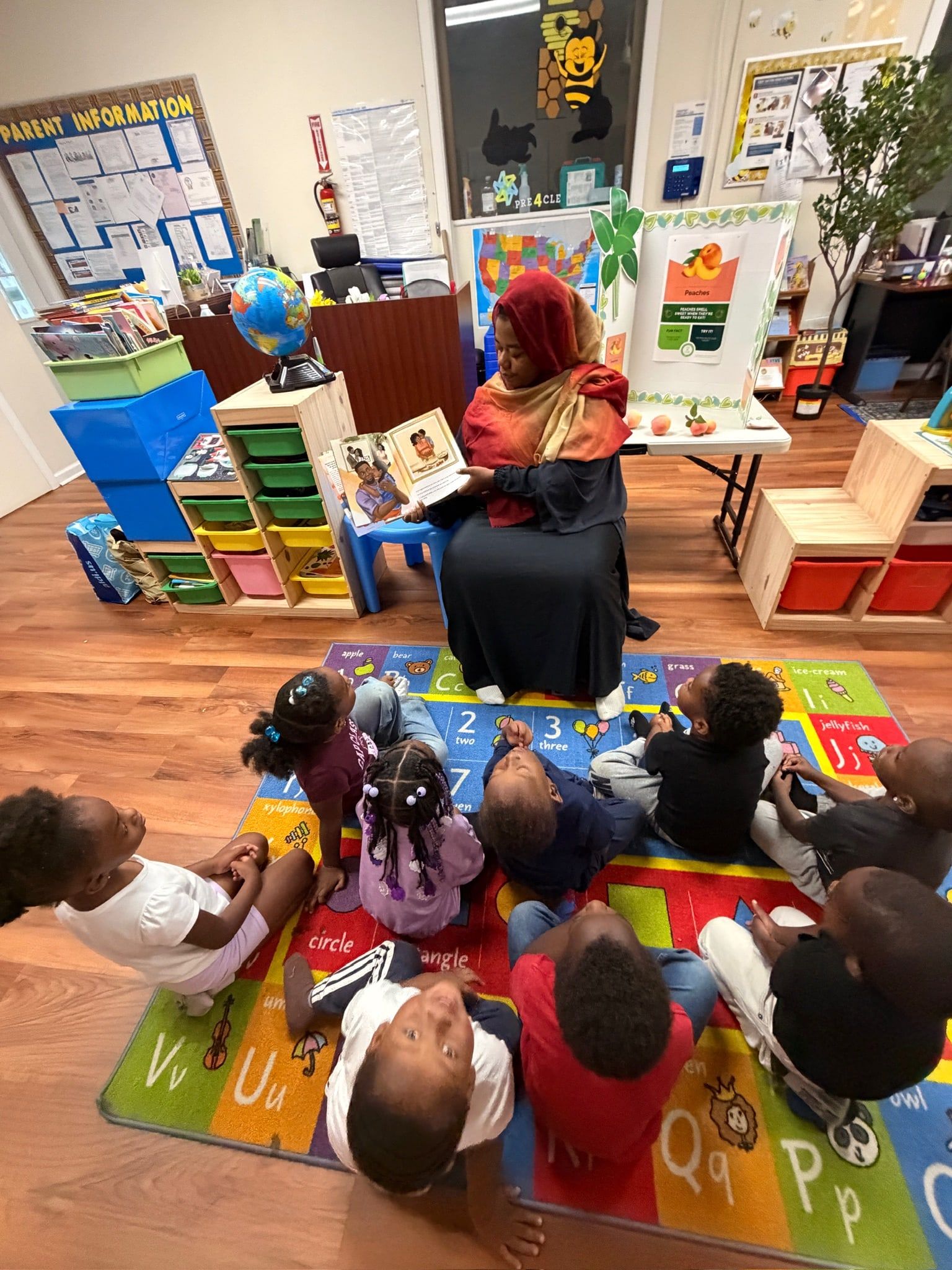 A picture book read aloud to children sitting on the alphabet rug