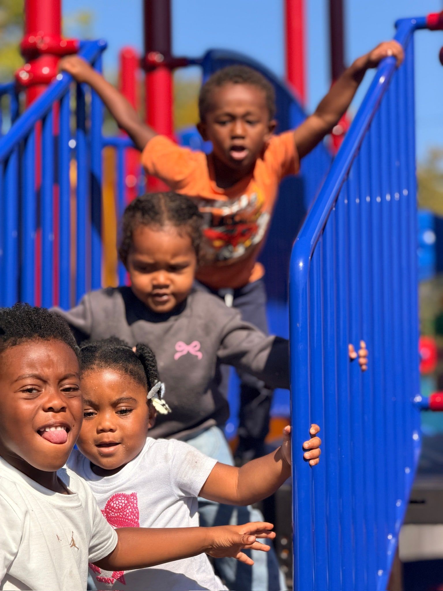 Four children climbing and grinning on the blue playground stairs