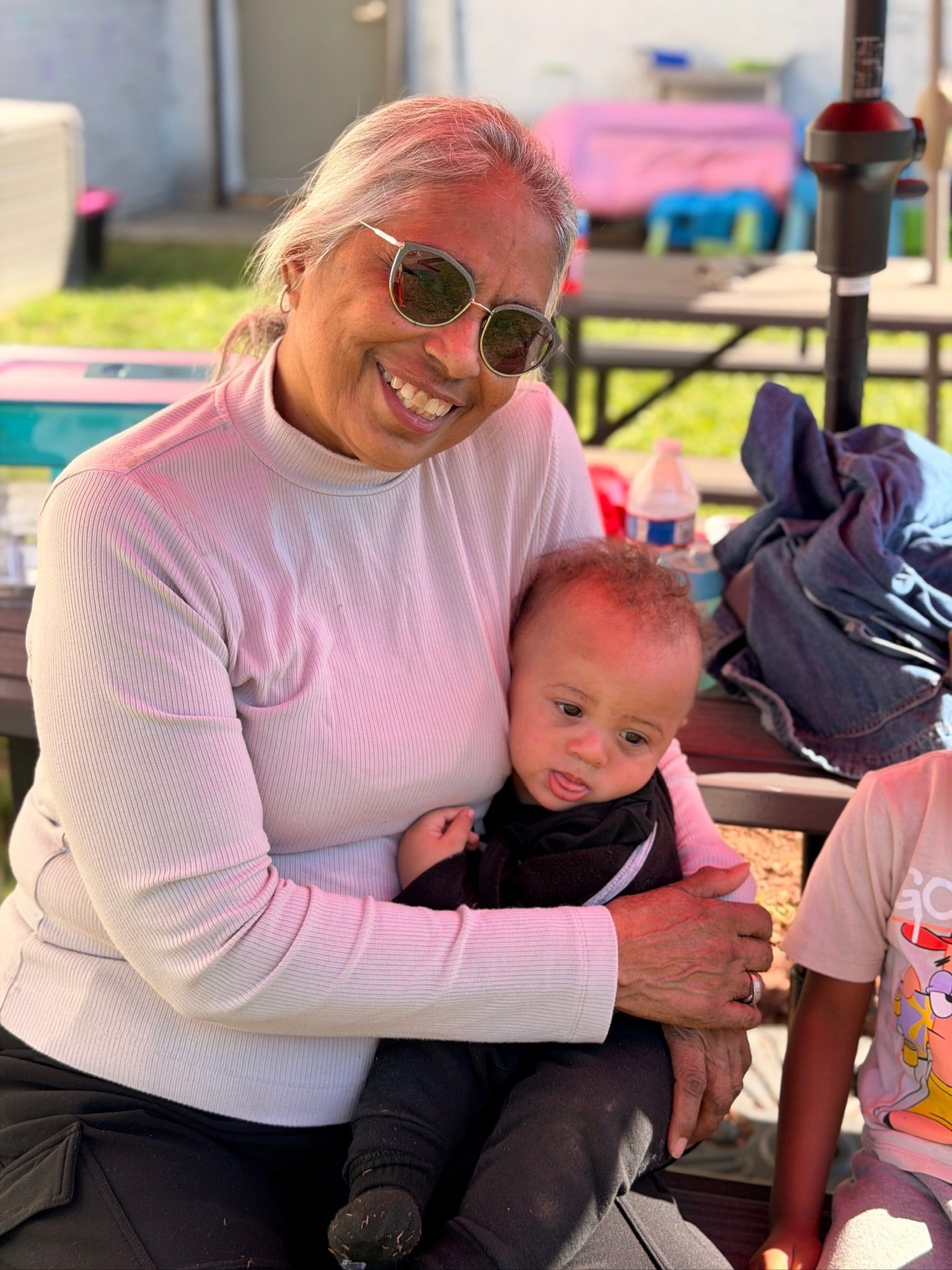 A smiling woman holding a baby on her lap outdoors