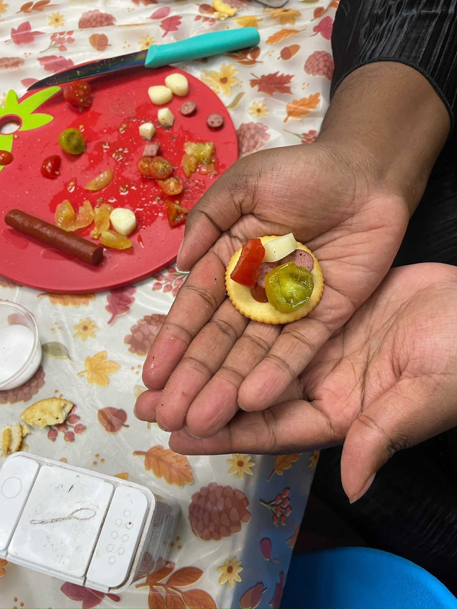 A hand holding a cracker topped with a tiny snack, beside a cutting board